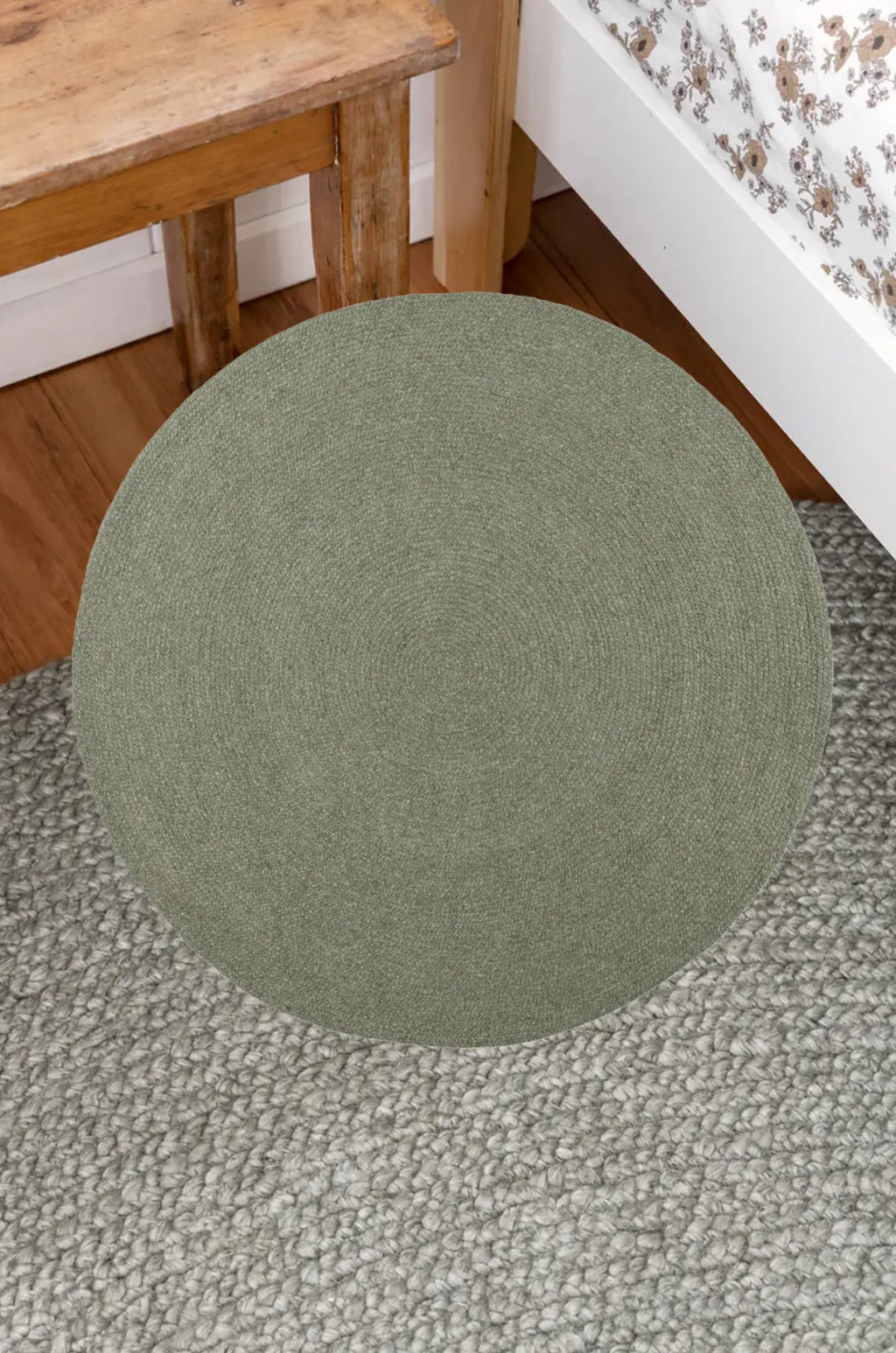 Round green rug on a textured floor with a wooden stool in the background.