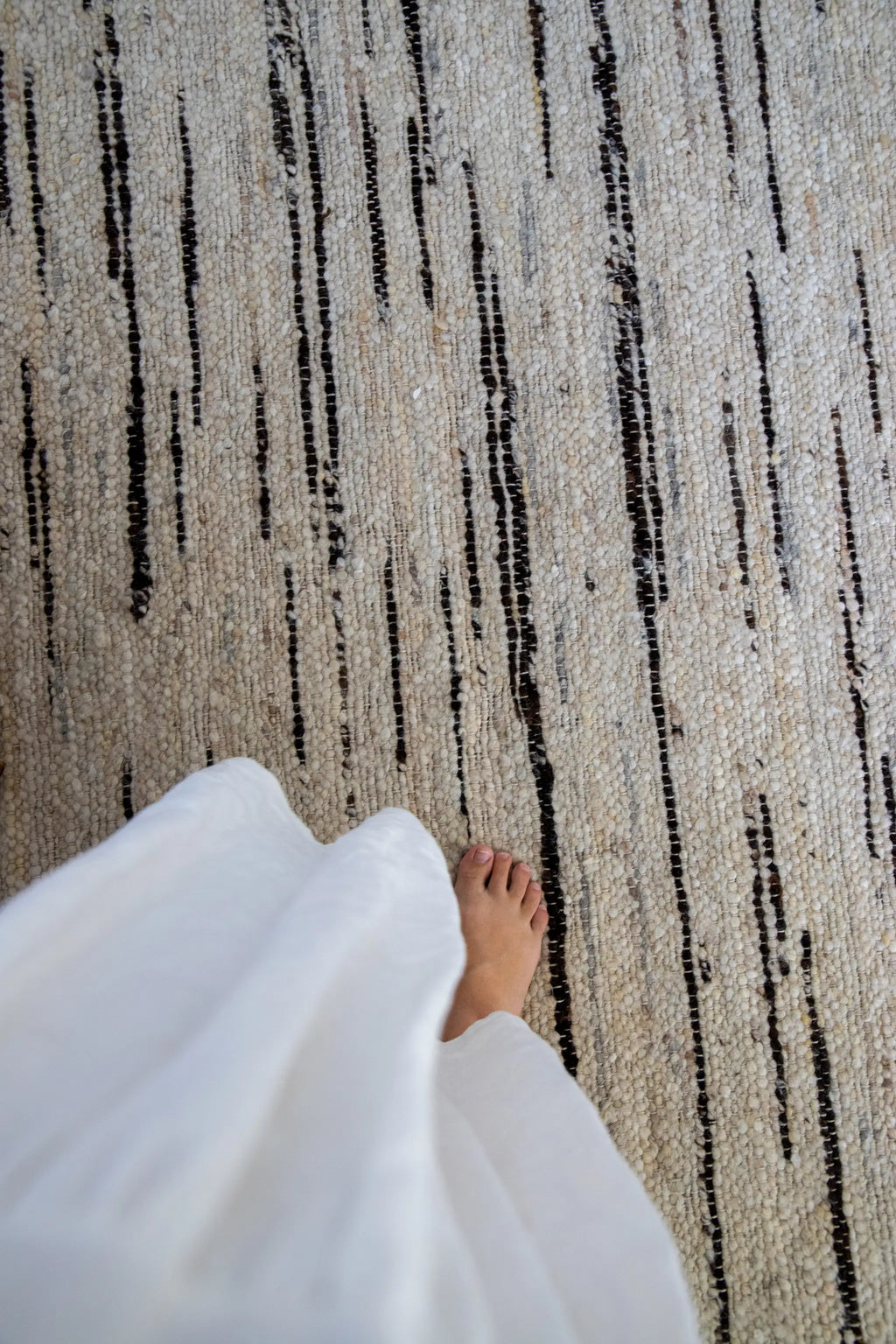 Person wearing a white dress standing on a textured beige and chocolate brown black striped rug from Rugs for Good.