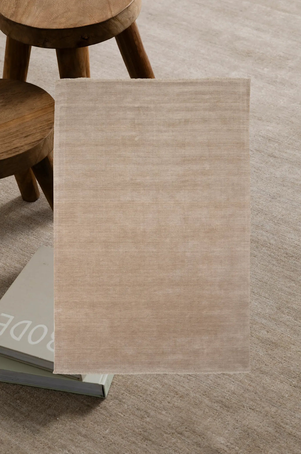 Beige rug on a carpeted floor with wooden stools in the background