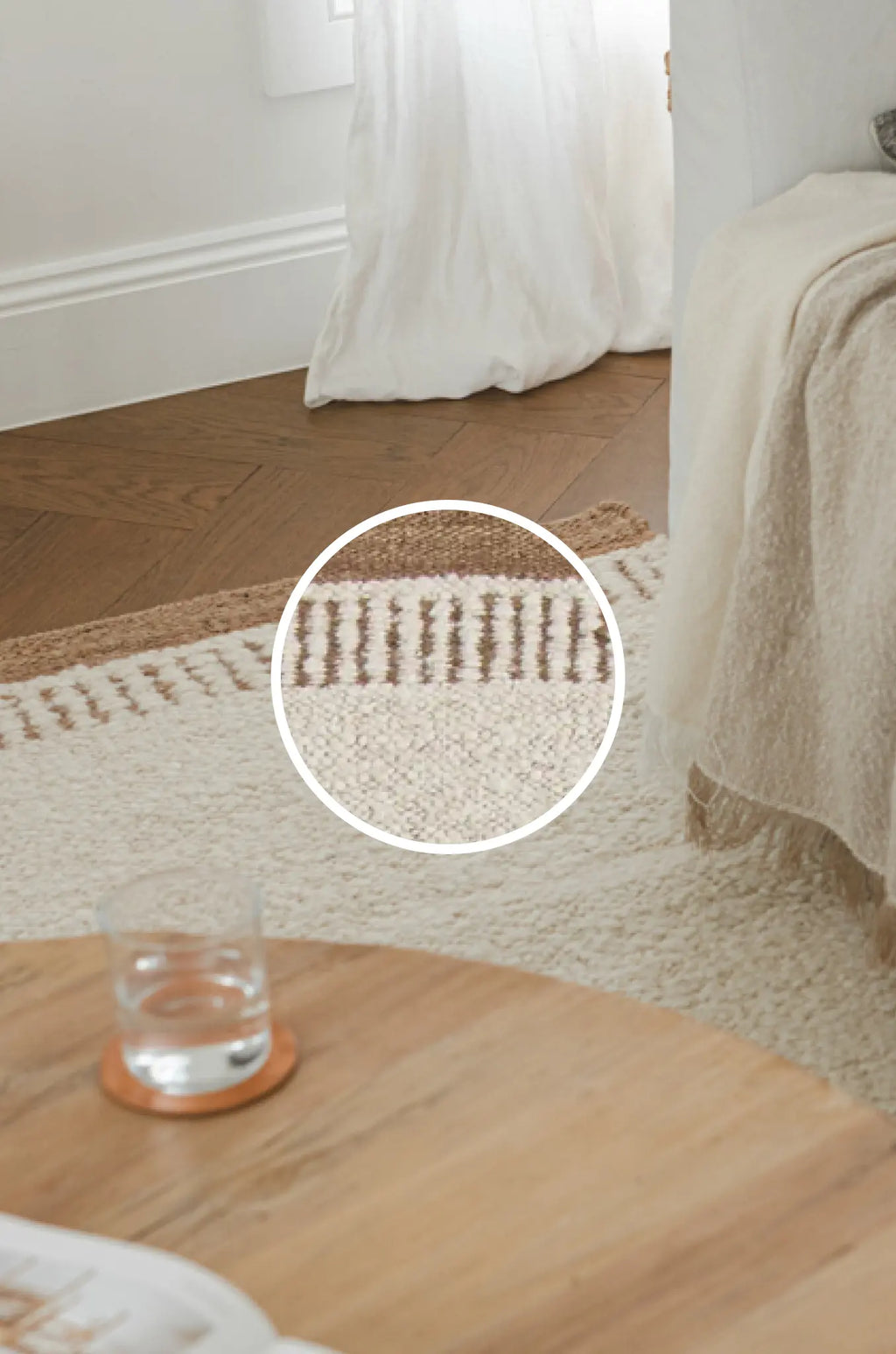 Close-up of a textured rug with a glass of water on a wooden floor.